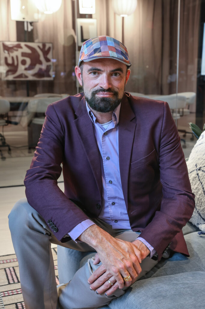 Graham Marsden seated in a jacket and wearing a colorful hat.